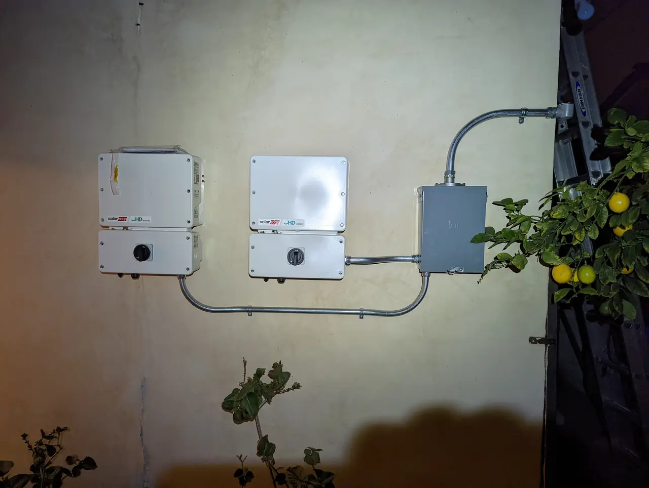 Two solar inverters and a junction box mounted on an exterior wall at dusk, North Hollywood