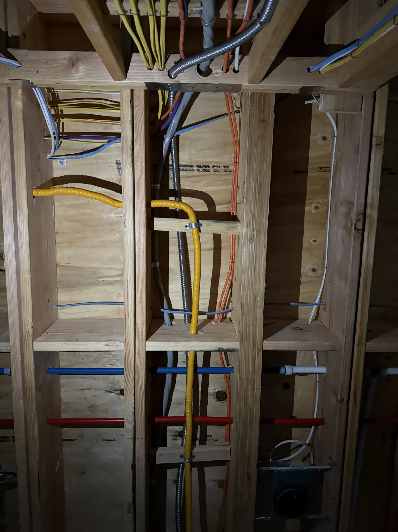 Electrical conduit and cable run through open wall studs beside plumbing in a building under construction, North Hollywood