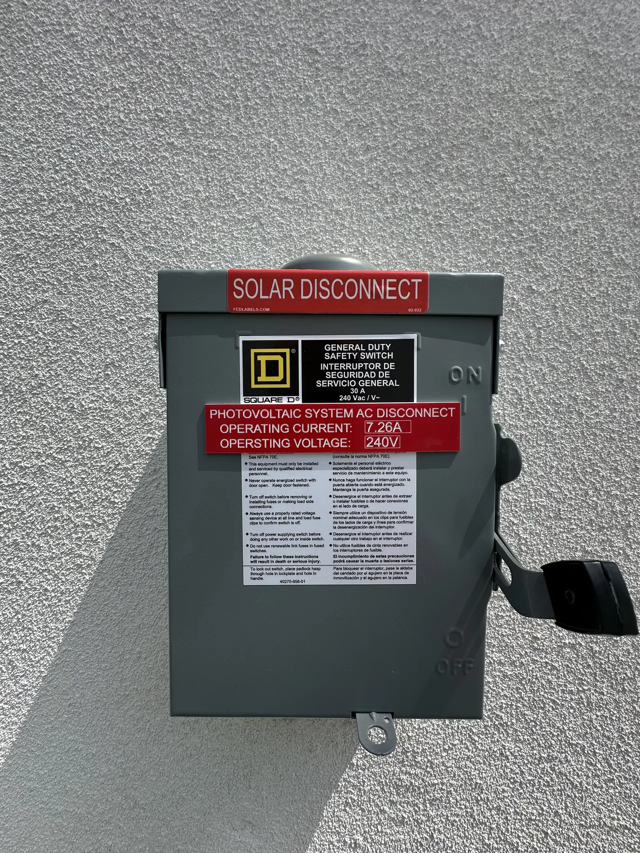 Photovoltaic AC disconnect switch on a stucco wall with a red operating-current placard, North Hollywood