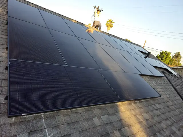 A large black solar array running up a shingle roof to the ridge against a clear sky, North Hollywood