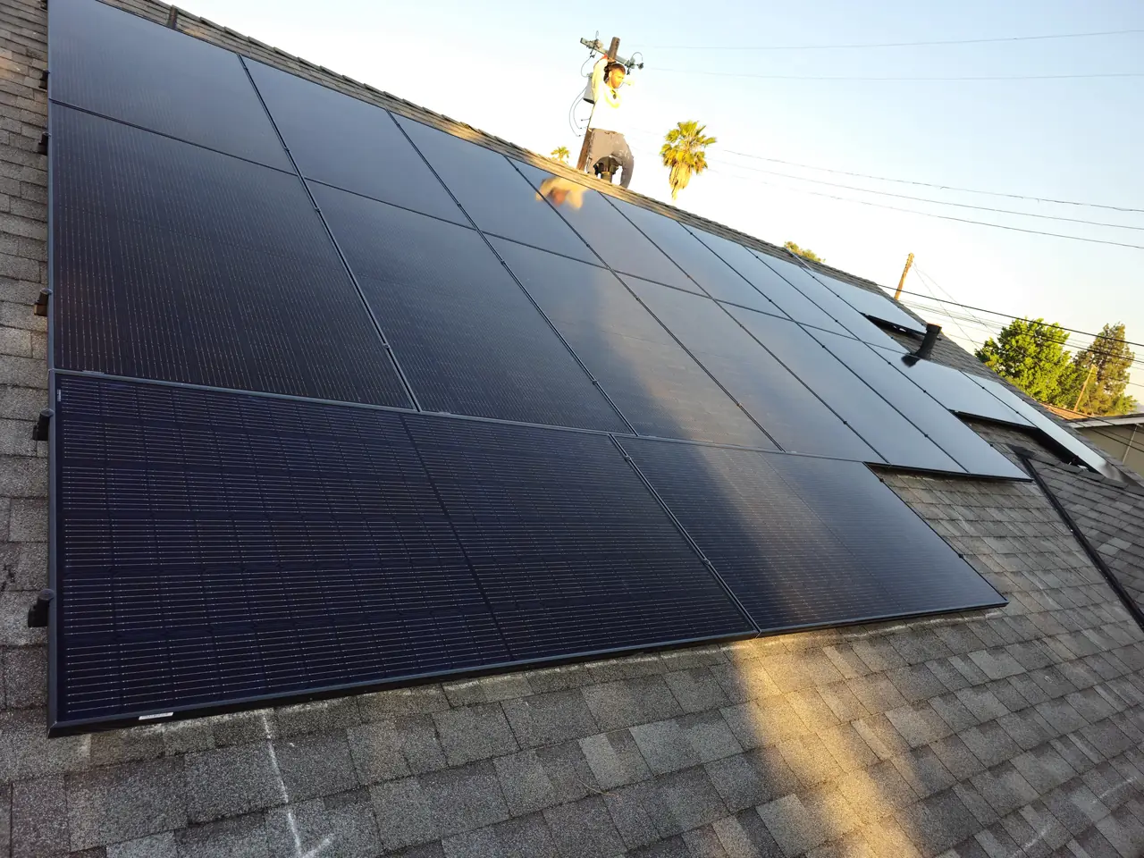A large black solar array running up a shingle roof to the ridge against a clear sky, North Hollywood