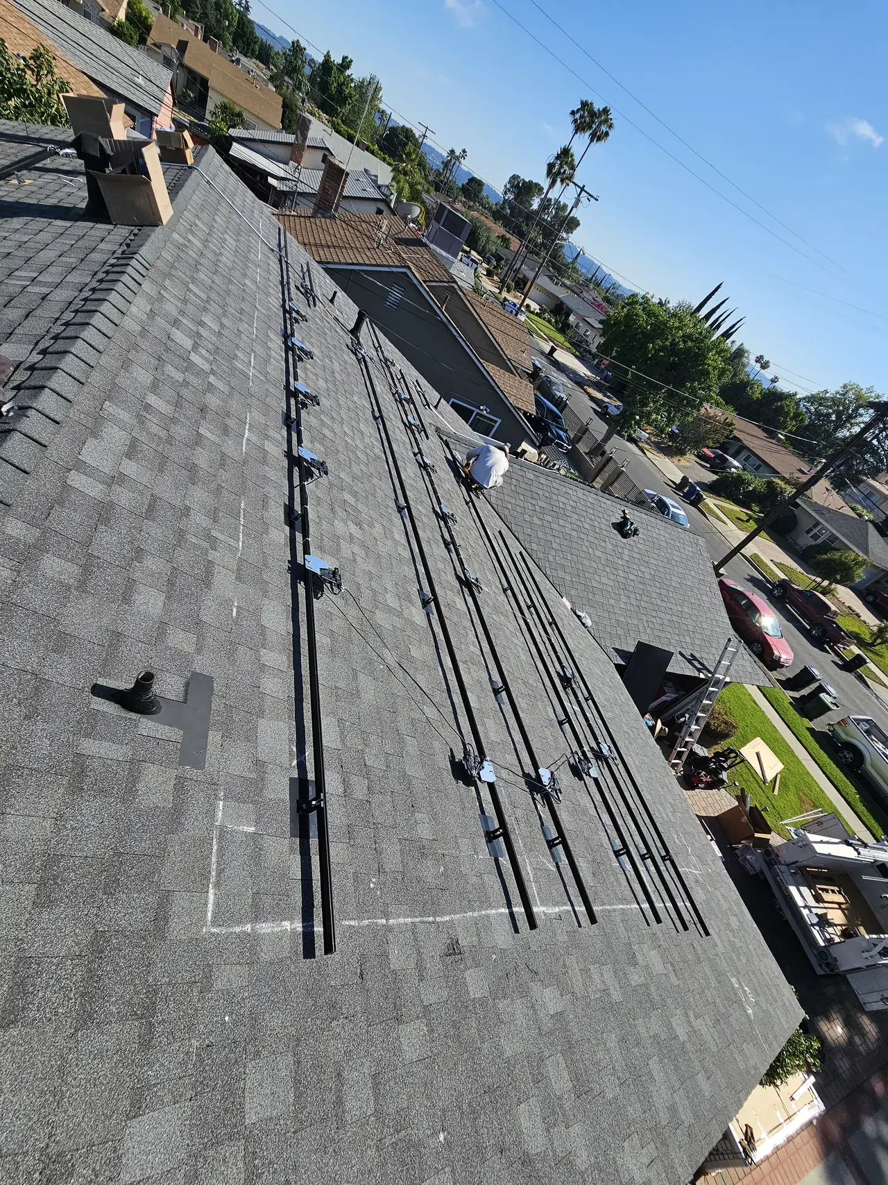 Solar racking rails and conductors laid out across a new composition shingle roof before the modules go on, North Hollywood