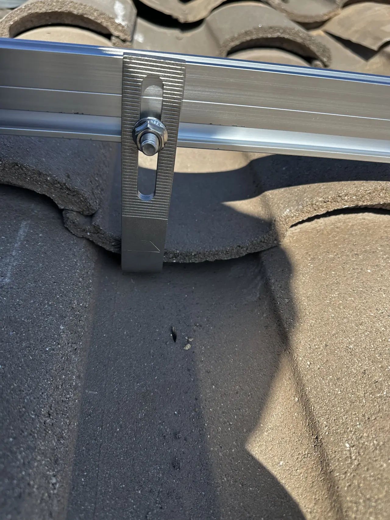 A metal tile hook carrying a mounting rail above intact concrete tiles, North Hollywood