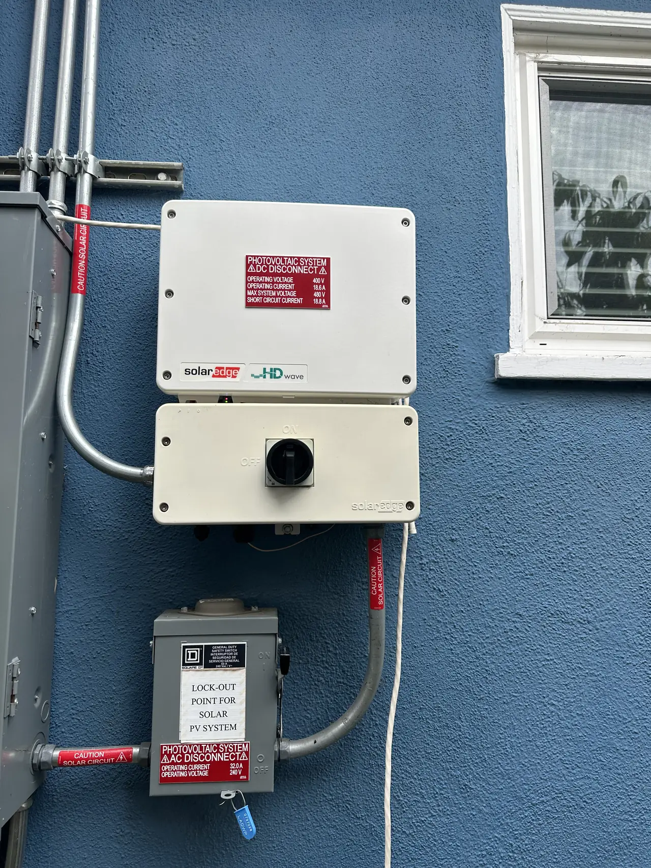 String inverter and AC disconnect mounted on a blue stucco wall, Northridge