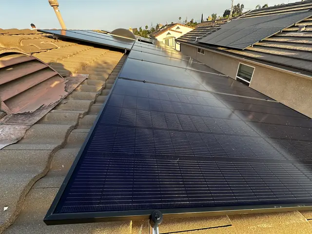 All-black solar modules running along a tan S-profile concrete tile roof with neighboring rooftops beyond, Pacoima, Los Angeles