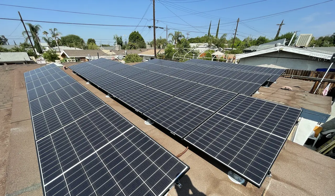 Rows of solar modules on tilt frames across a low-slope roof, seen along the array, Pacoima, Los Angeles