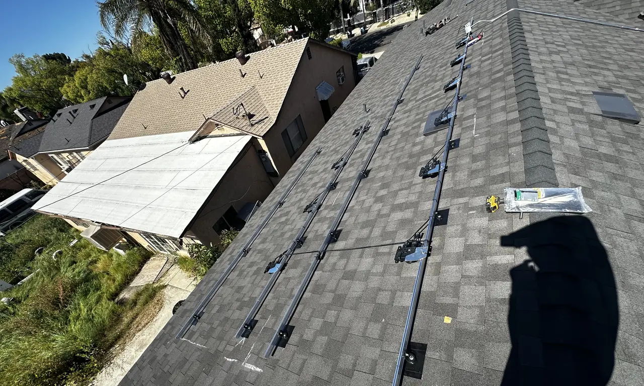 Mounting rails laid out along a bare gray composition shingle roof before the modules arrive, Pacoima, Los Angeles