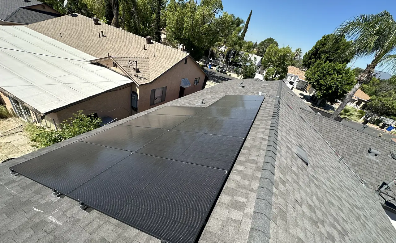 A completed run of all-black solar modules along a gray composition shingle plane, seen from above, Pacoima, Los Angeles
