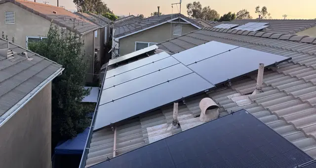 Solar modules on a brown concrete tile roof at dusk with a neighboring rooftop beyond, Pacoima, Los Angeles