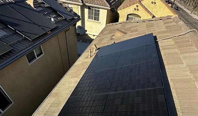 An all-black solar array on a composition shingle plane, with a tile-roofed neighboring house beyond, Pacoima, Los Angeles
