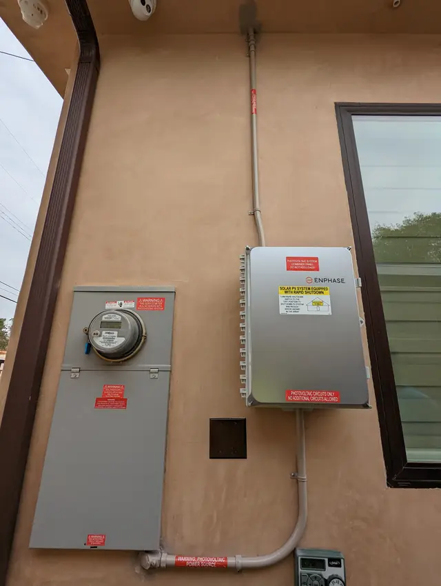 A meter enclosure and a closed Enphase combiner panel mounted side by side on a tan stucco wall, Panorama City