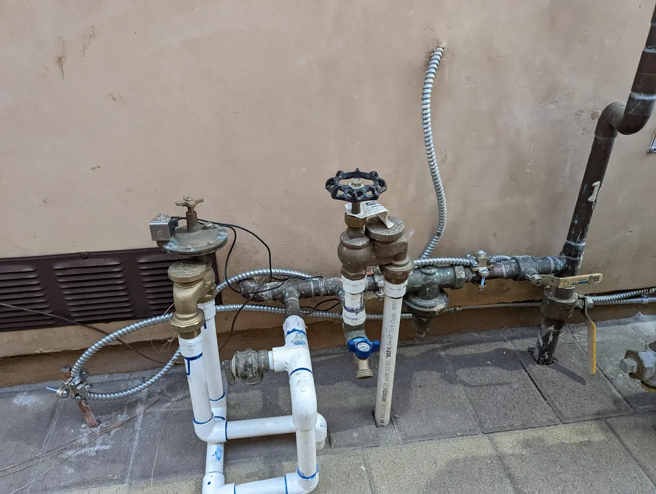A gas service manifold at the base of a stucco wall with flexible metal conduit and a bonding jumper run across it, Panorama City