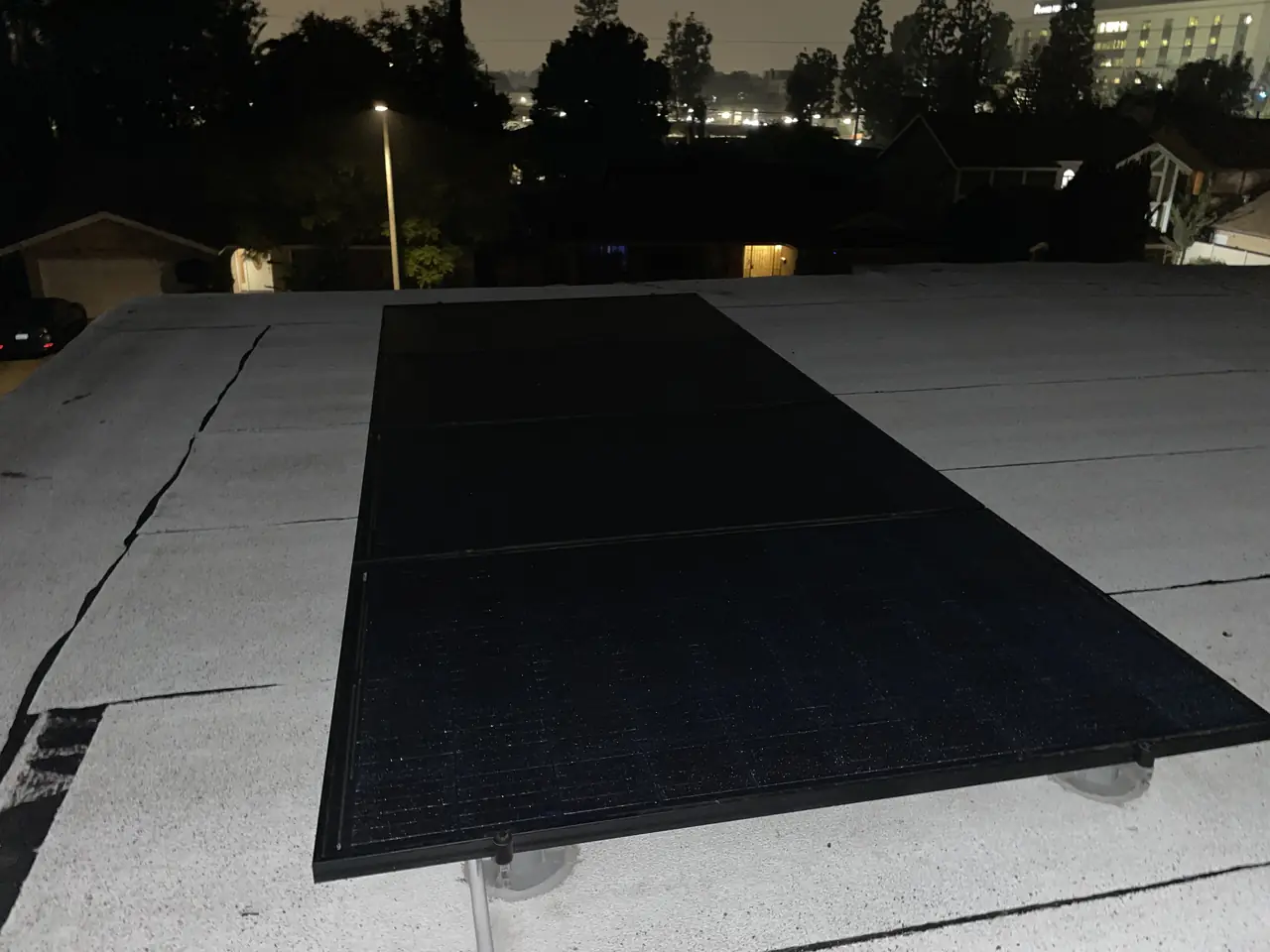 A single black module on the white low-slope roof with the neighborhood beyond at dusk, Panorama City
