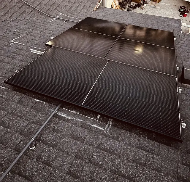 Black solar modules set across a brown composition shingle roof at the end of the day, with a work vehicle in the driveway below, Panorama City