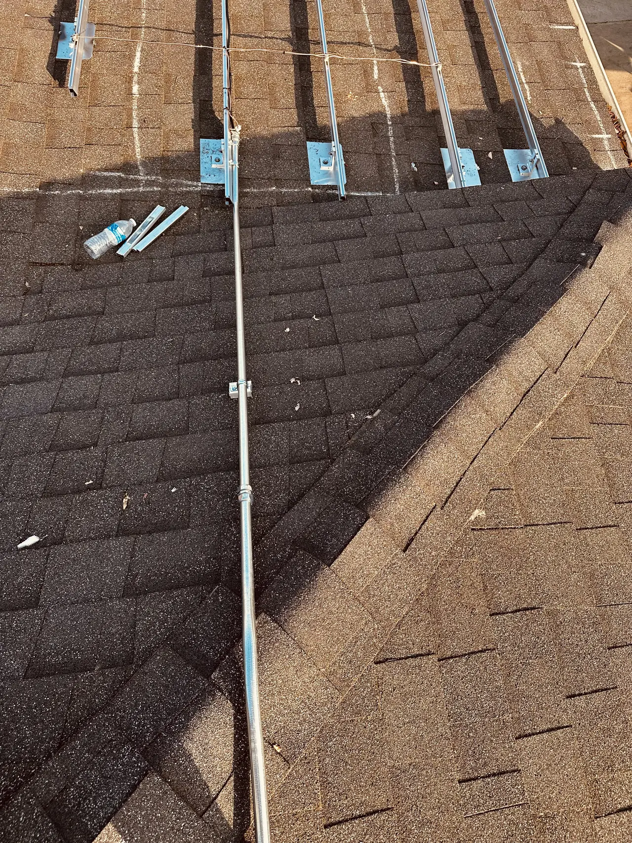Aluminum standoffs and rails laid out across a brown composition shingle roof with the conduit run beside them, Panorama City