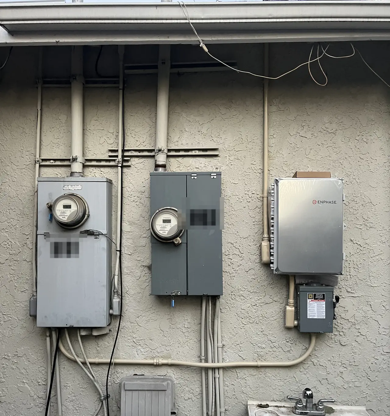Two meter enclosures and a closed Enphase combiner panel mounted in a row along a stucco wall under a soffit, Panorama City