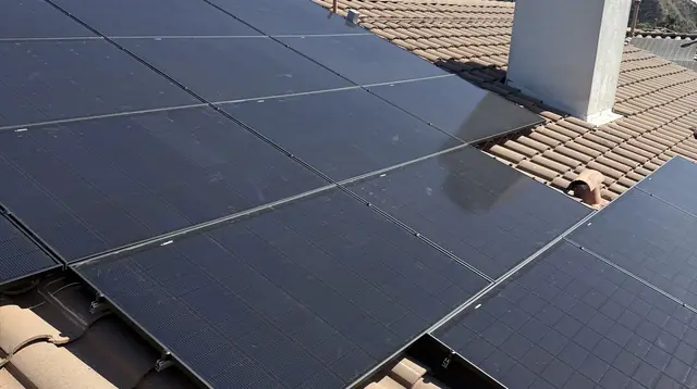 A solar array around a chimney on a tile roof with mountains behind, Porter Ranch