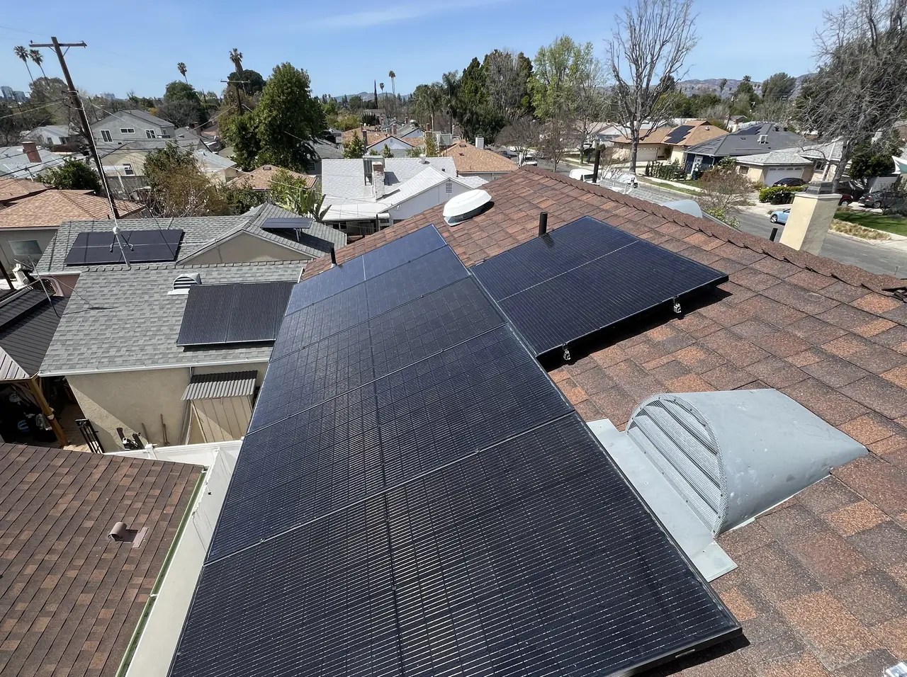Finished black solar modules on a brown composition shingle roof with the neighborhood beyond, Reseda