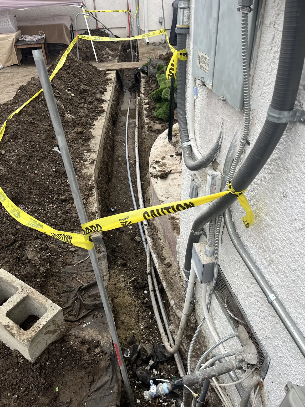 Detail of the open trench where flexible conduit rises out of the ground and enters the wall beside the service equipment, Reseda