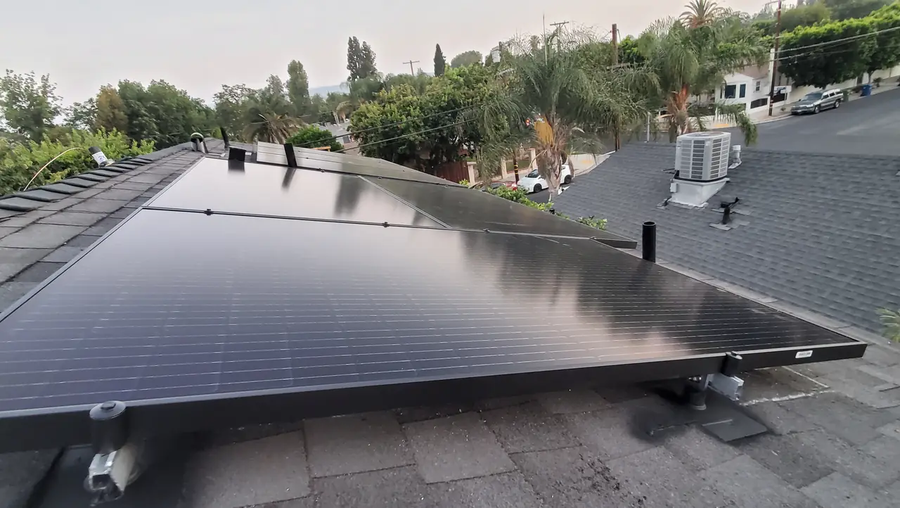 Black solar modules across a shingle roof with the street and neighboring rooftops beyond, Reseda