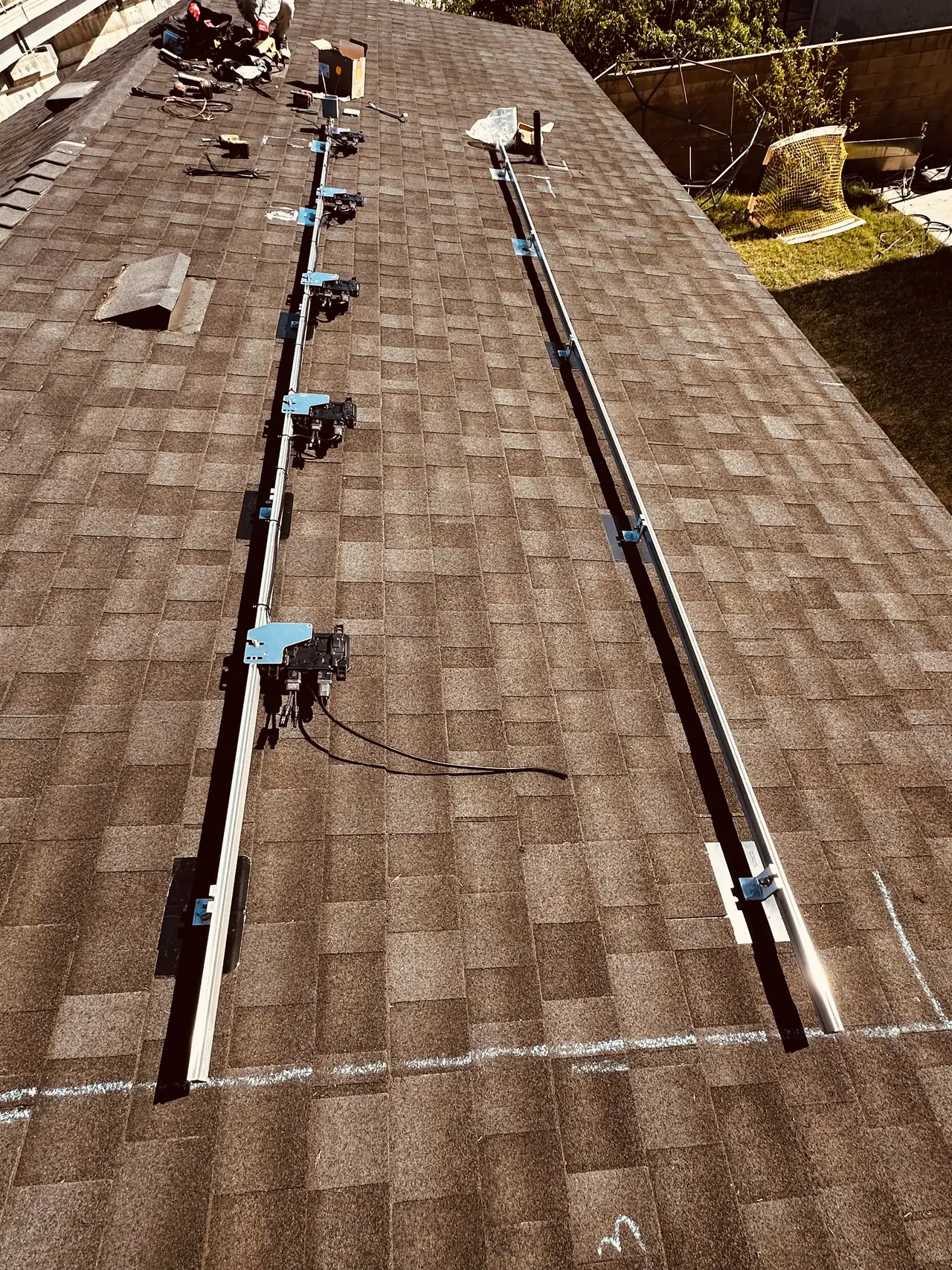 Two mounting rails with microinverters attached, set out along a shingle roof before the modules go on, Reseda