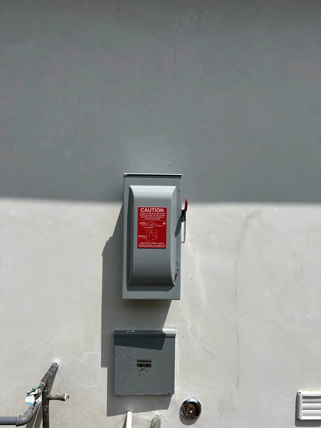 A gray fused AC disconnect with a red handle mounted on the exterior wall of the new unit, Reseda