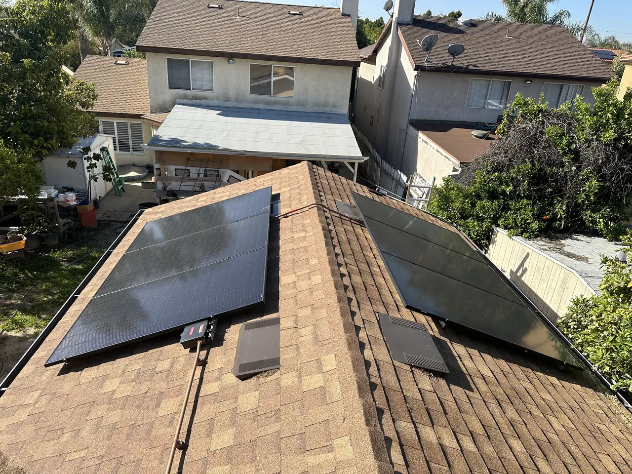 Black solar modules on two facing planes of a shingle roof with a two-story stucco house behind, Reseda