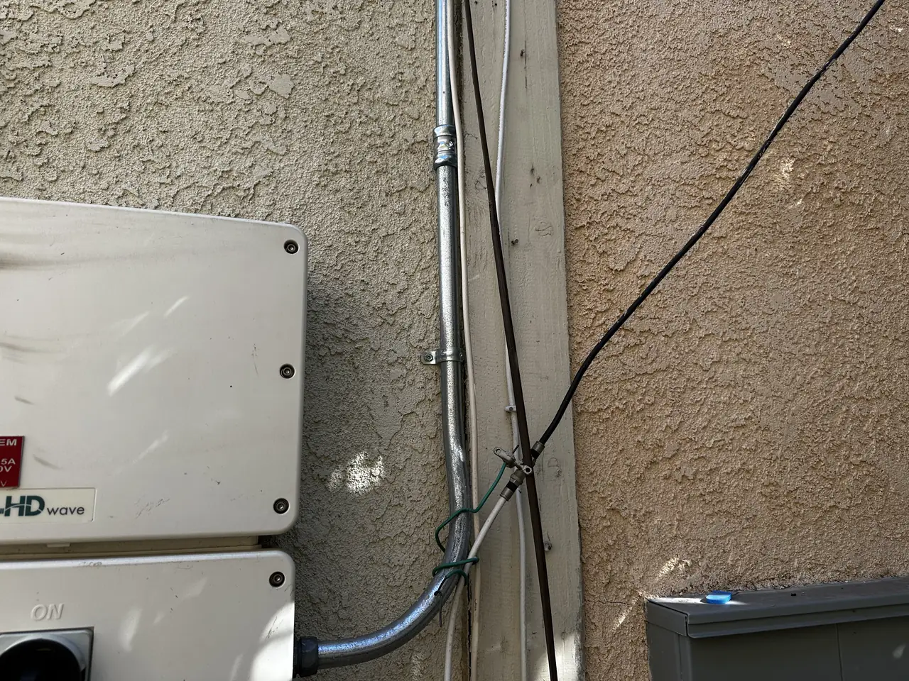 A white SolarEdge inverter mounted on a stucco wall with conduit running up beside it, Reseda
