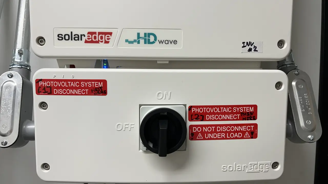 A SolarEdge HD-Wave inverter with its photovoltaic disconnect and warning placards, San Fernando