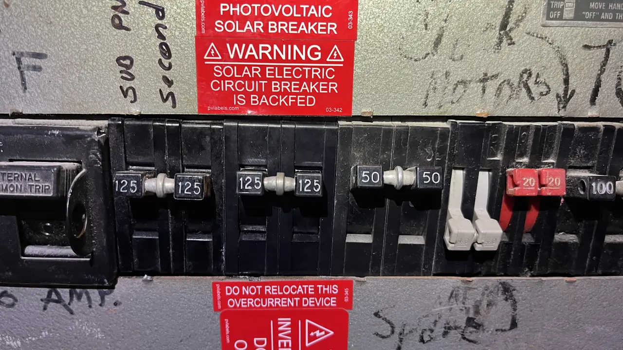 A backfed solar breaker with red photovoltaic warning placards in a commercial panel, San Fernando