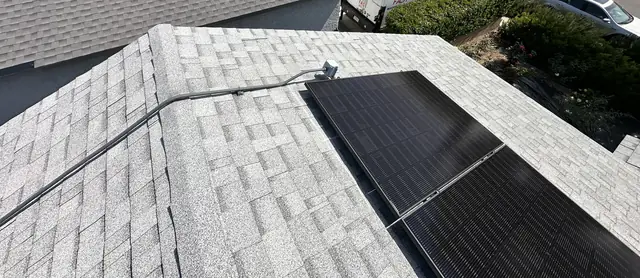 Eight black solar modules on a gray shingle roof face, with a conduit run across the roof, San Fernando