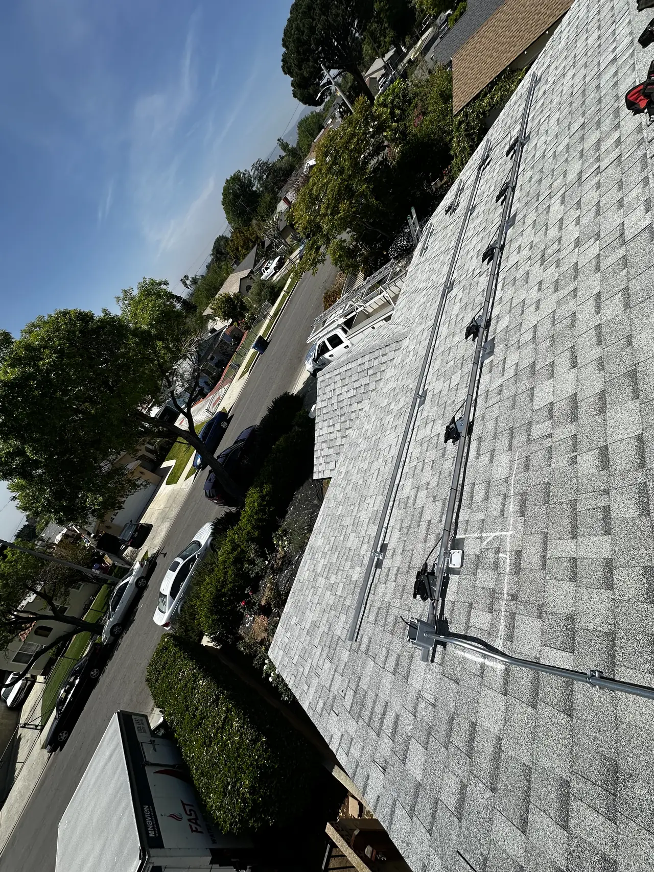 Aluminum rails with Enphase microinverters clipped on, laid across a shingle roof before the modules, San Fernando