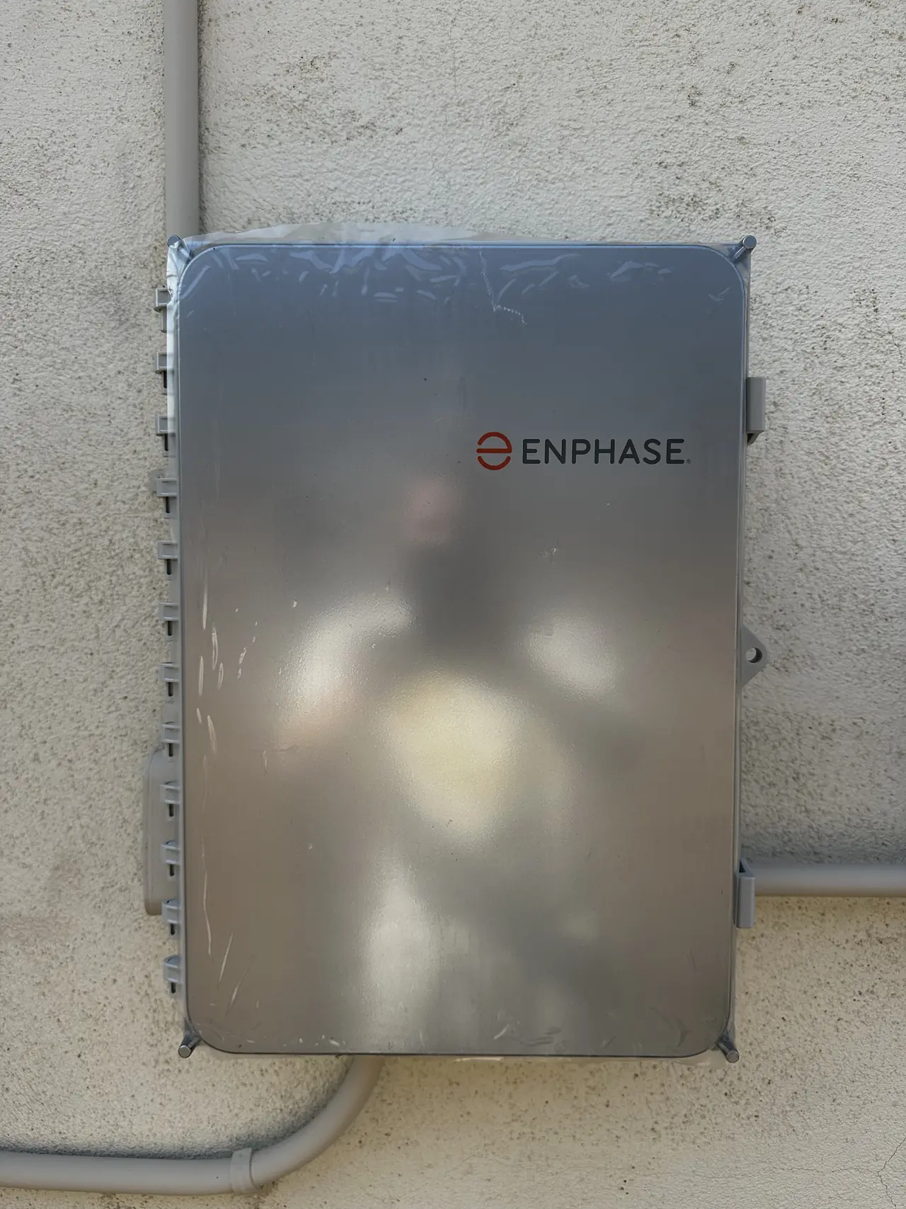 An Enphase combiner box mounted on a stucco wall with conduit entering from below, San Fernando