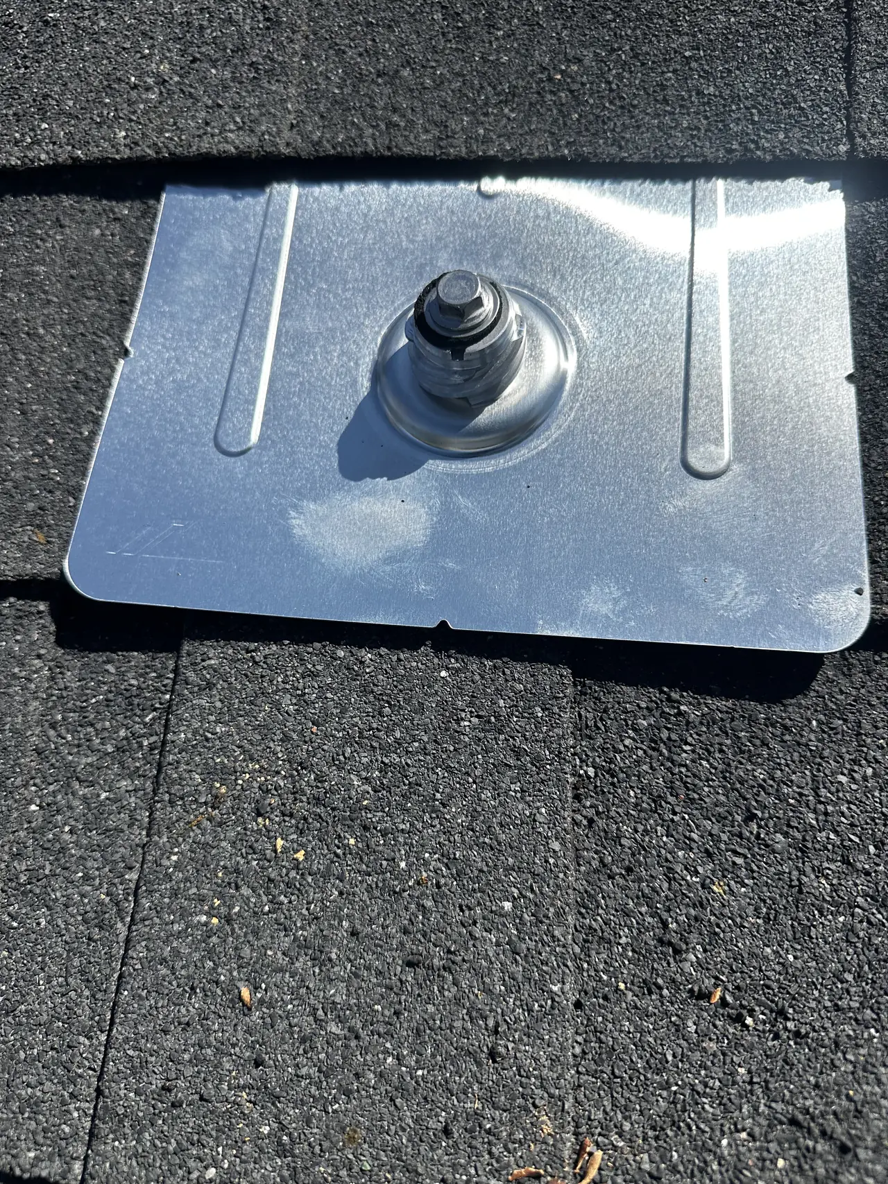A metal flashing plate fixed over a solar mount with its bolt tightened, on a shingle roof, San Fernando
