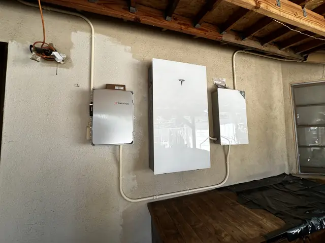An Enphase combiner, a Tesla Powerwall and a Tesla gateway side by side on a stucco wall under a patio roof, San Fernando