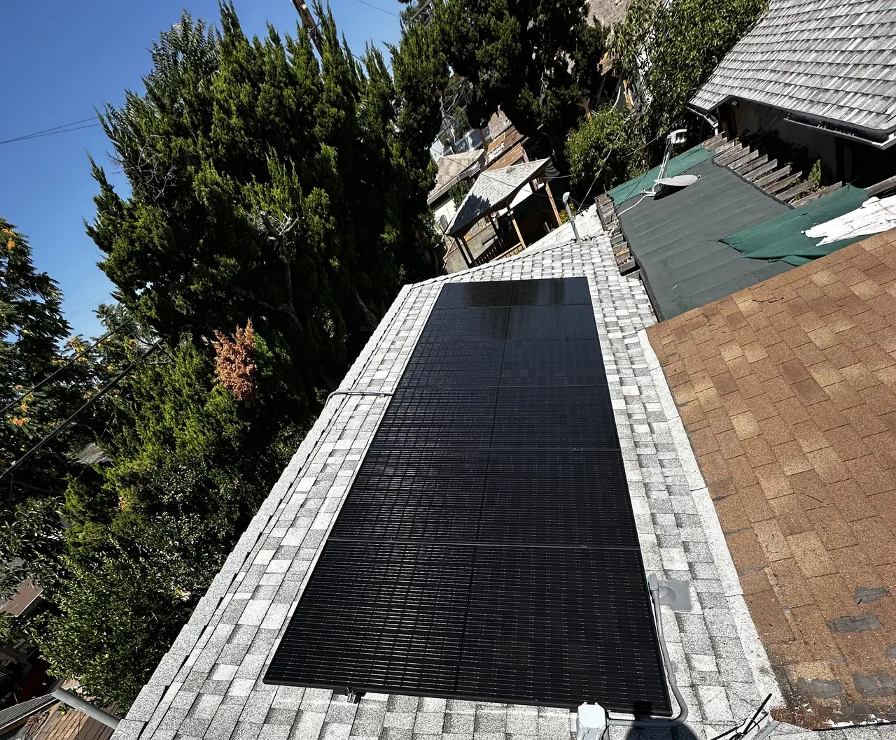 A long row of black solar modules along one face of a gray shingle roof, San Fernando