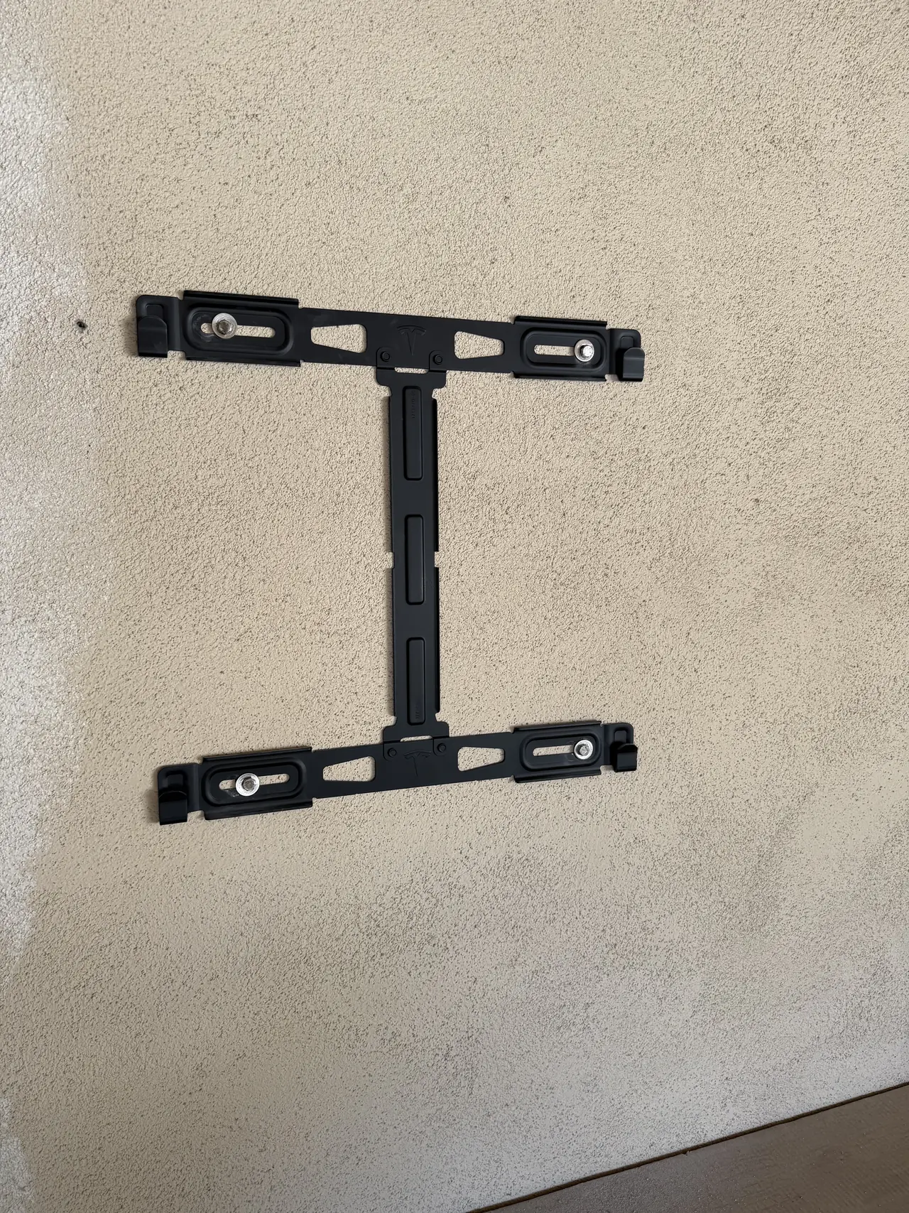 A black battery mounting bracket fixed to a stucco wall before the battery is hung, San Fernando