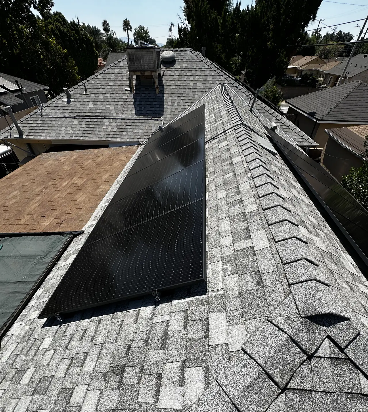 Black solar modules on another face of a gray shingle roof with a ridge running alongside, San Fernando