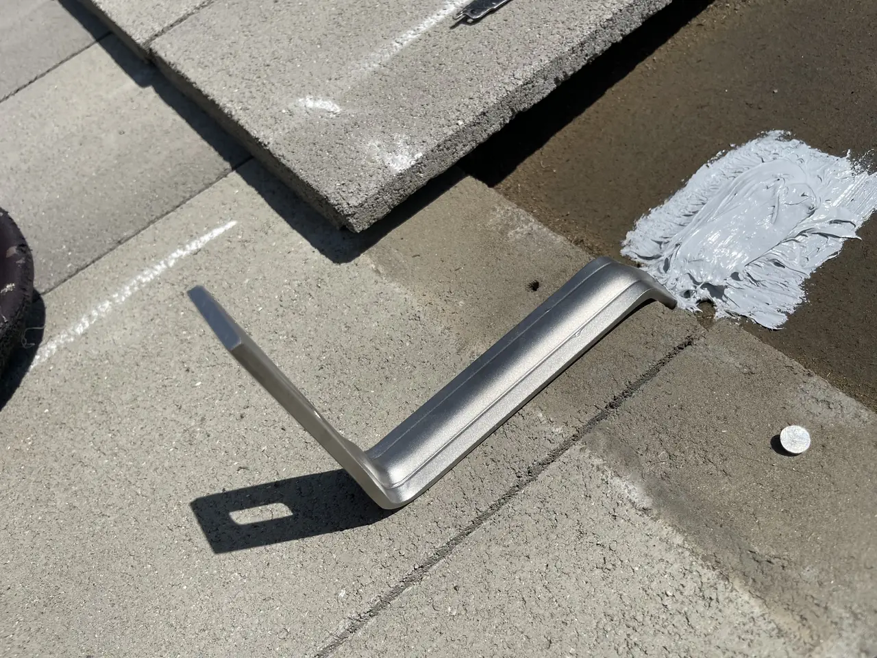 A steel tile hook fixed on the underlayment with sealant over its fasteners, beside a lifted concrete tile, San Fernando