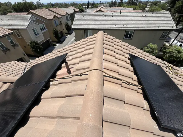 Two solar arrays on clay S-tile on either side of a roof ridge, with a conduit crossing the ridge between them, San Fernando