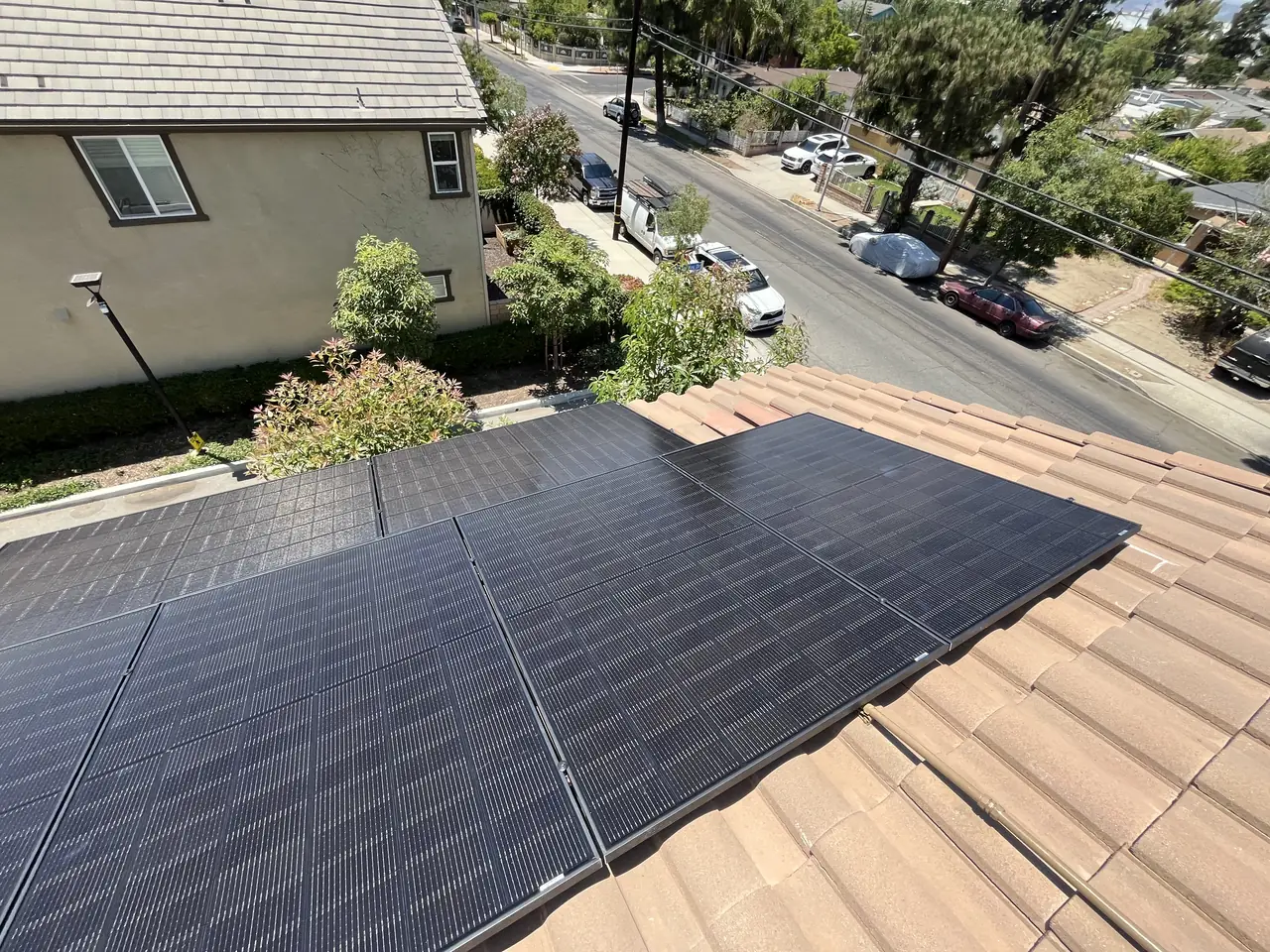 An array of black solar modules on a clay S-tile roof above a residential street, San Fernando