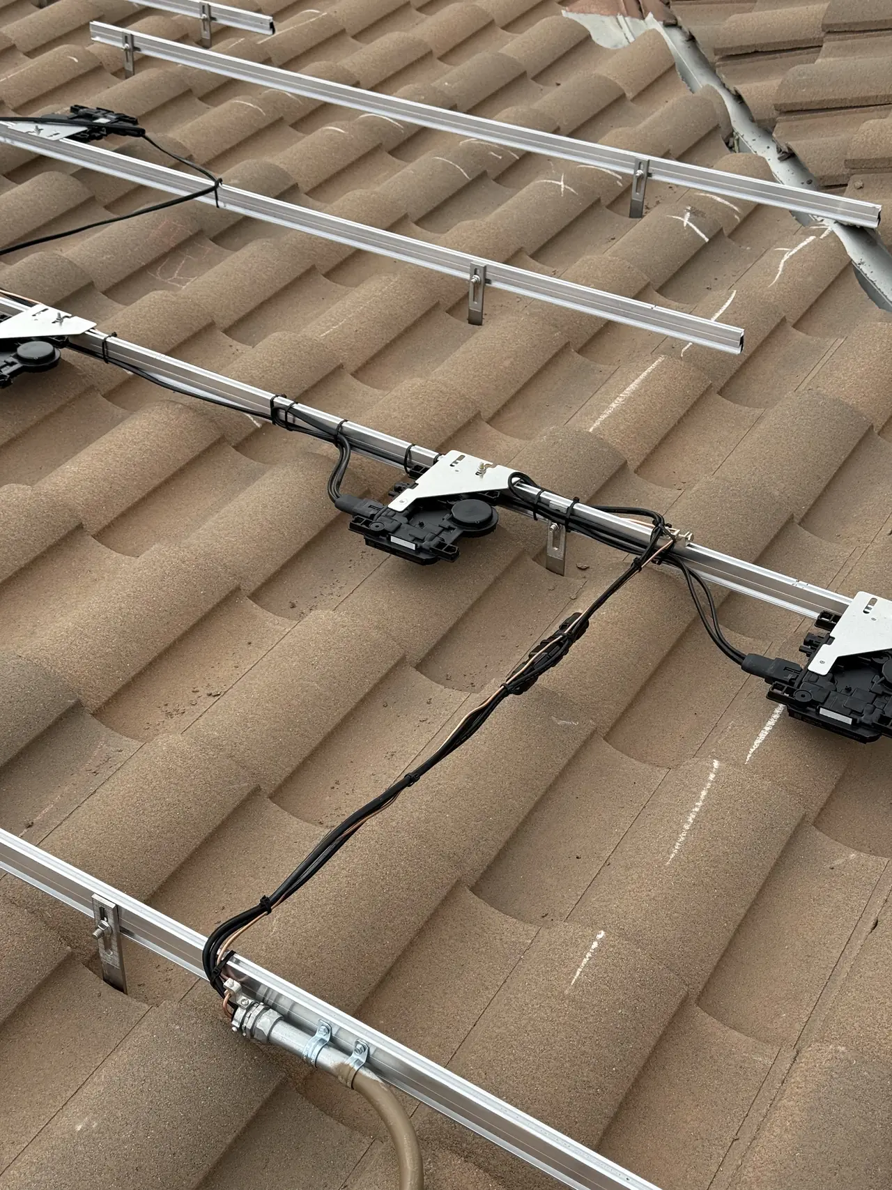 Aluminum rails with Enphase microinverters and their trunk cable above a clay S-tile roof, San Fernando