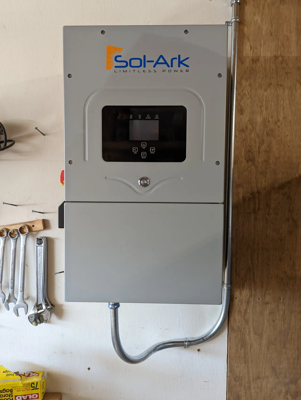 A closed Sol-Ark hybrid inverter on a garage wall with conduit running up to the ceiling, Santa Clarita