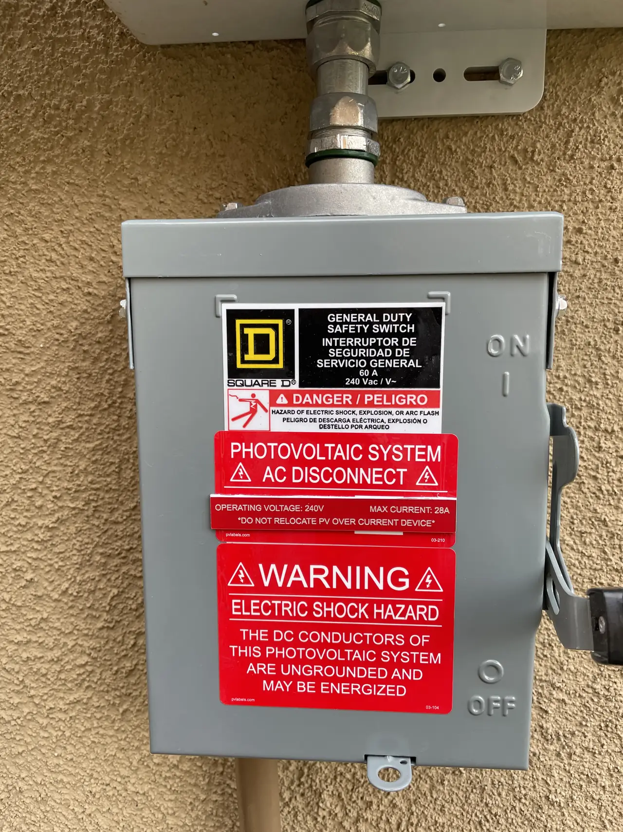 A closed general-duty safety switch with photovoltaic warning labels on a stucco wall, Santa Clarita