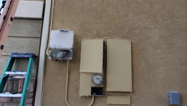 The side wall of a house carrying the solar equipment, with a ladder against the stucco, Santa Clarita