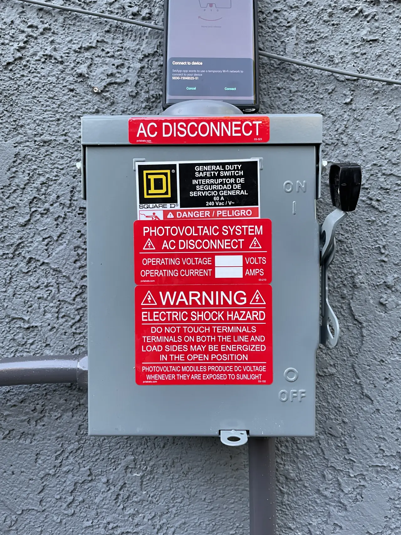 A closed alternating-current disconnect with photovoltaic warning labels on a stucco wall, Santa Clarita
