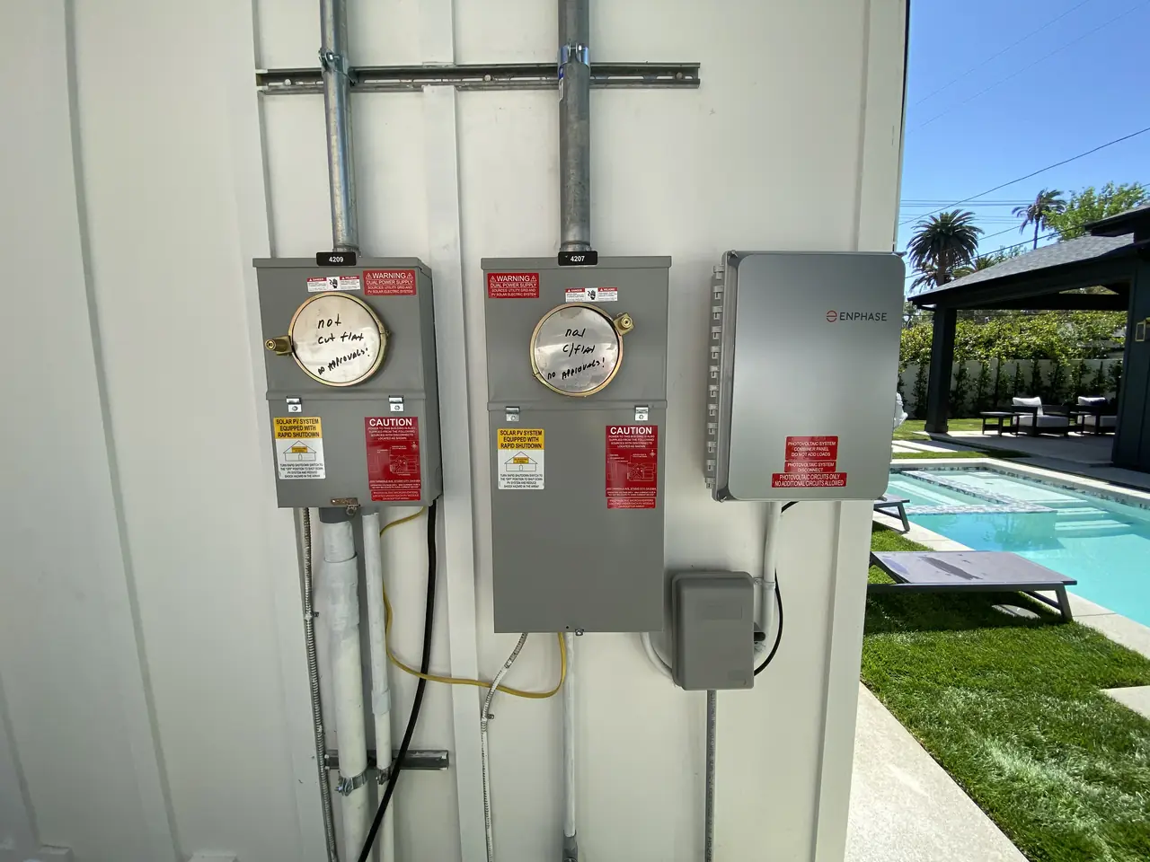Two meter sockets side by side on an exterior wall with a solar combiner beside them and a pool beyond, Studio City