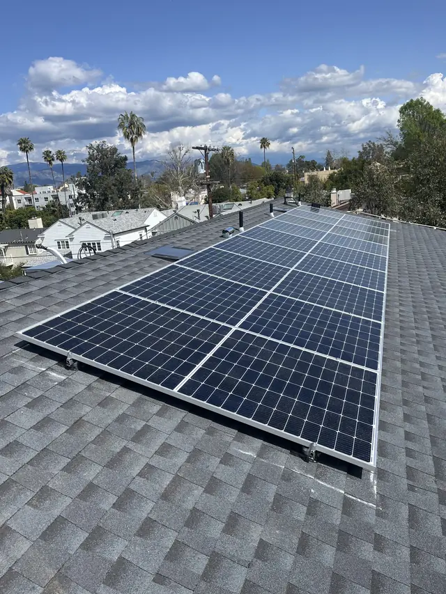 Solar array on a new composition shingle roof under a cloudy blue sky with the neighborhood beyond, Studio City