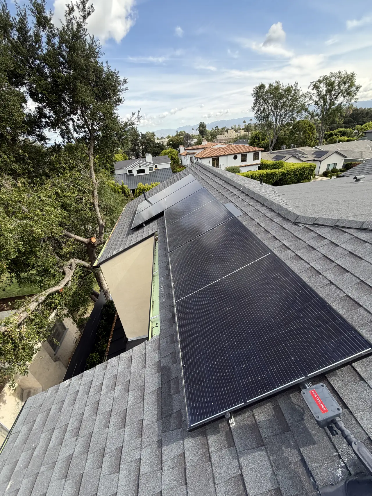 Solar array along a shingle roof with neighboring houses and trees beyond, Studio City