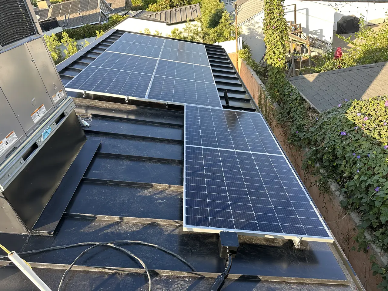 Solar modules on rails over a low-slope section of metal roof beside a rooftop air-conditioning unit, Studio City